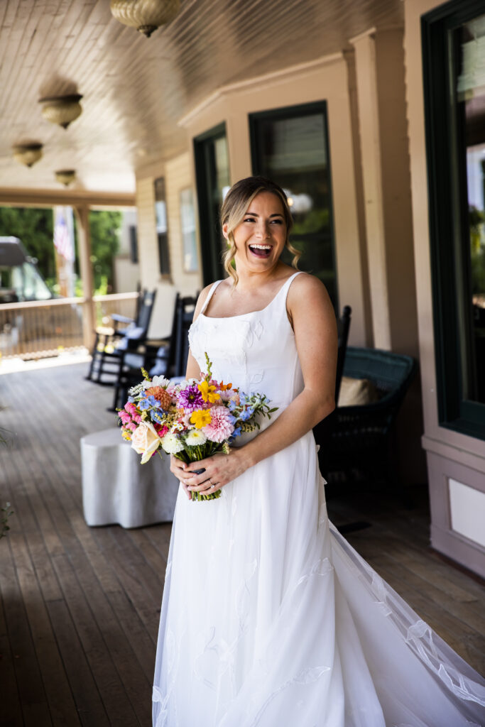 A woman in a white wedding dress holds a bouquet of flowers on a porch.