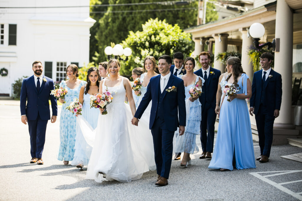A group of people in formal attire, including a bride and groom, walking down a street.