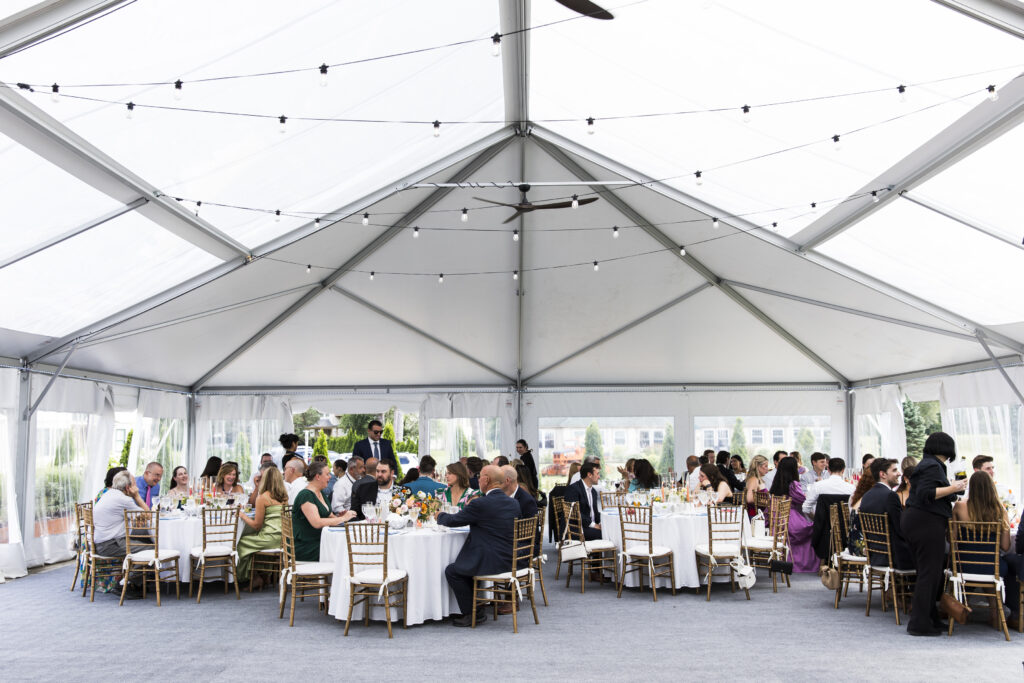 A group of people seated at tables in a white tent, engaged in a meal or event.