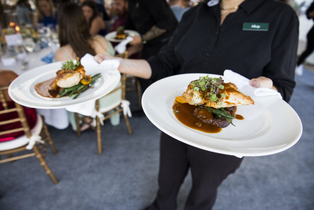 A person holding a plate of food with a table in the background.