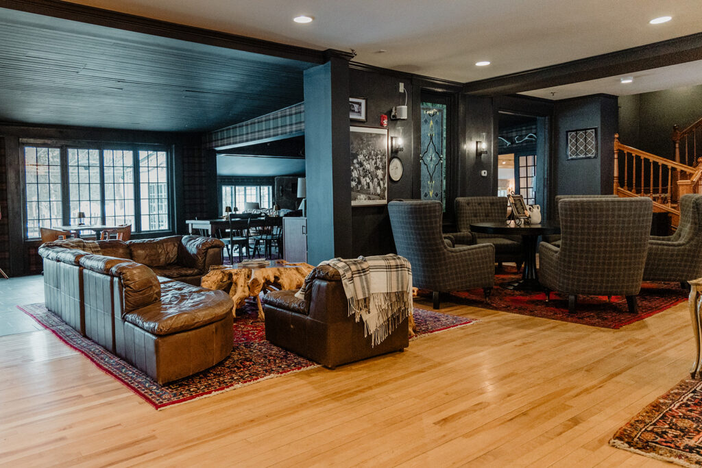 A spacious living room with a staircase, featuring a large window, a leather couch, a rug, and a wooden floor.